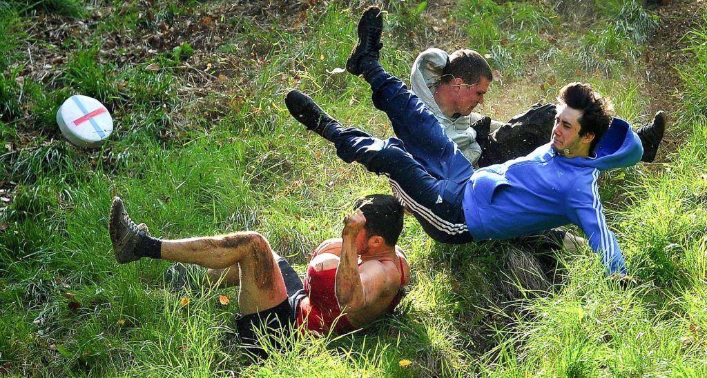 men fall down hill whilst rolling cheese