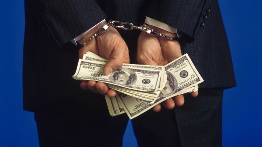 Someone handcuffed holding cash, representing the link between gambling and crime