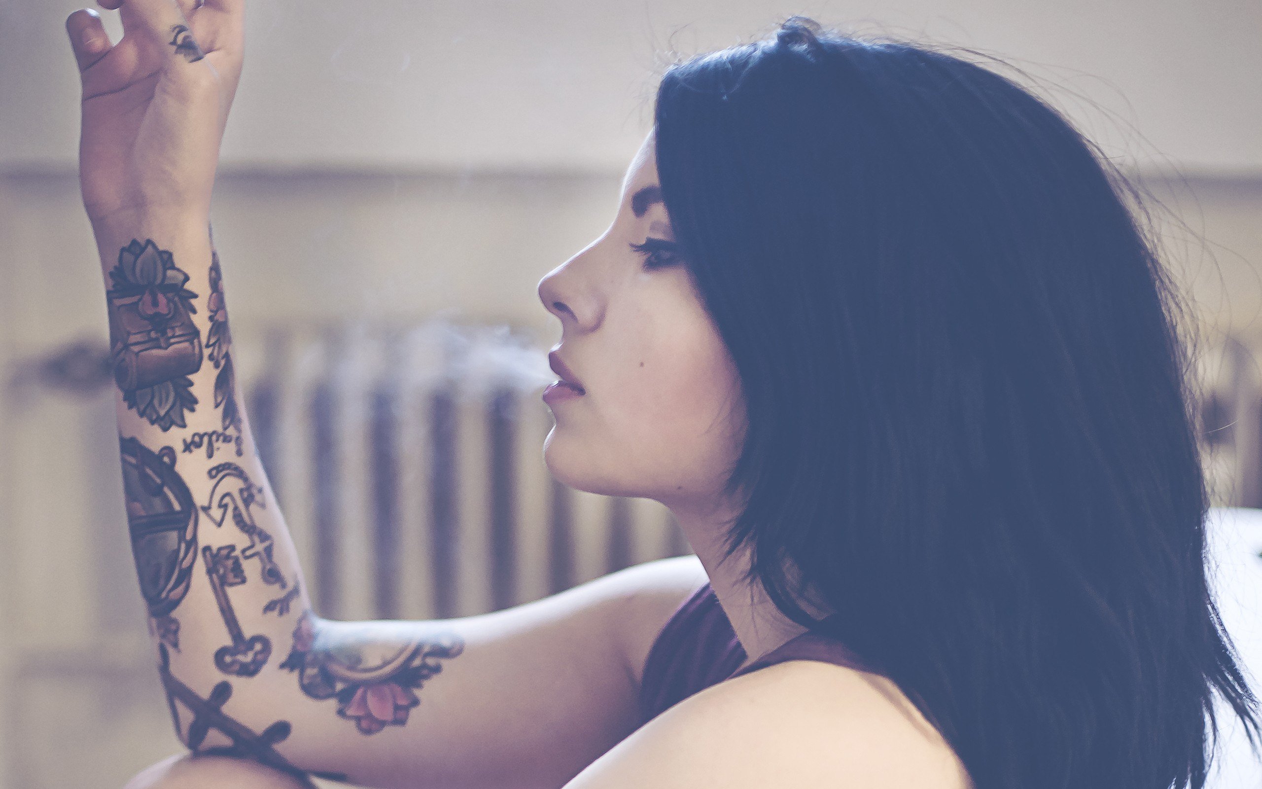 A girl smoking with half a tattoo sleeve