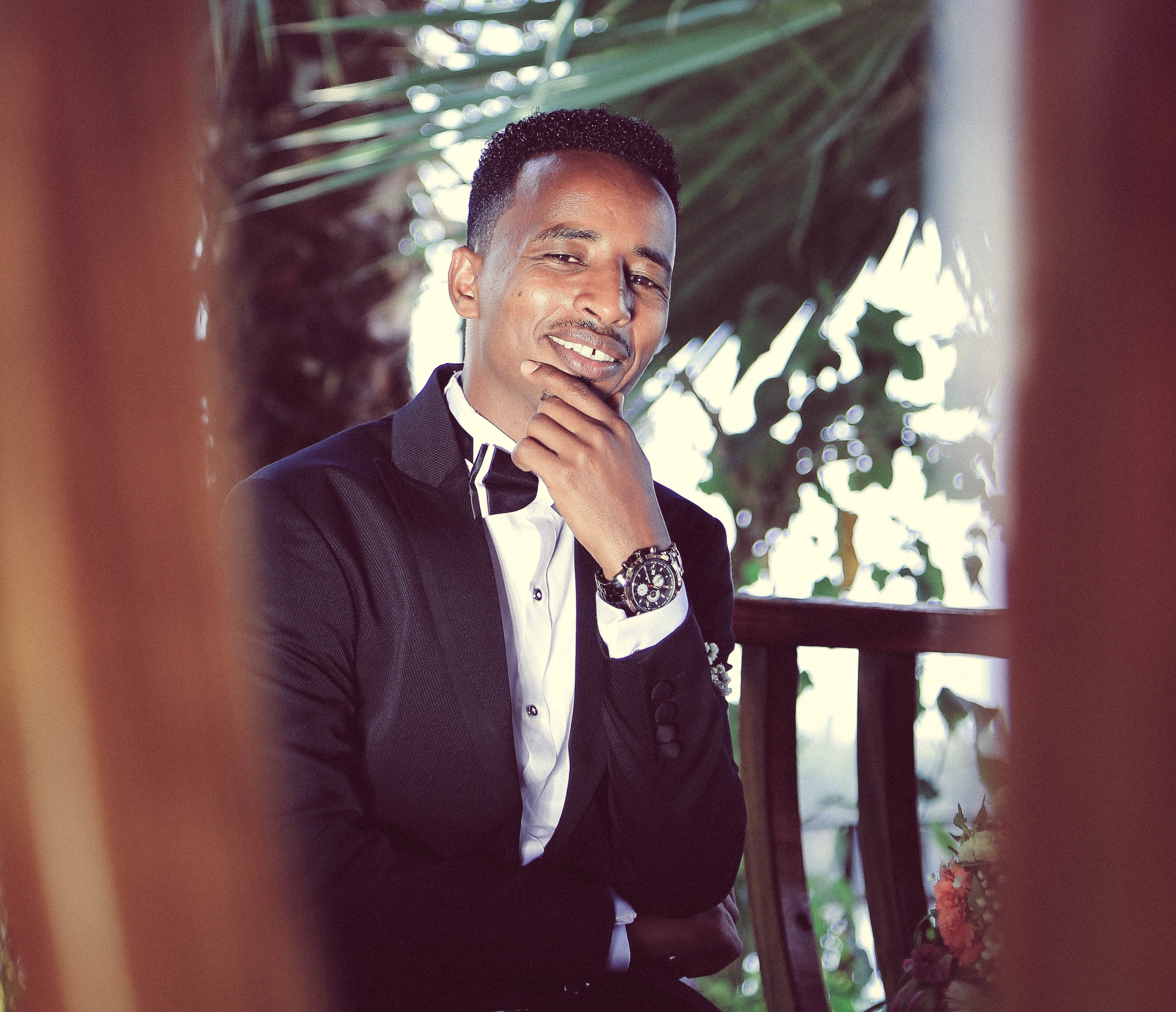 Man wearing tuxedo beside wooden fence