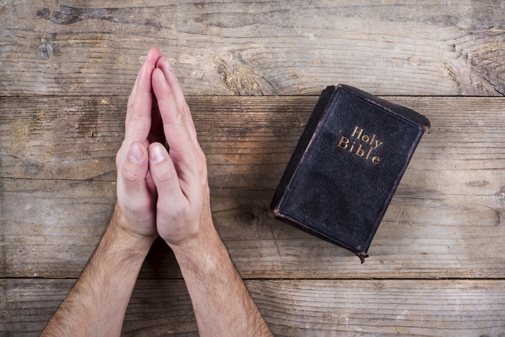 Bible and praying hands on wooden table