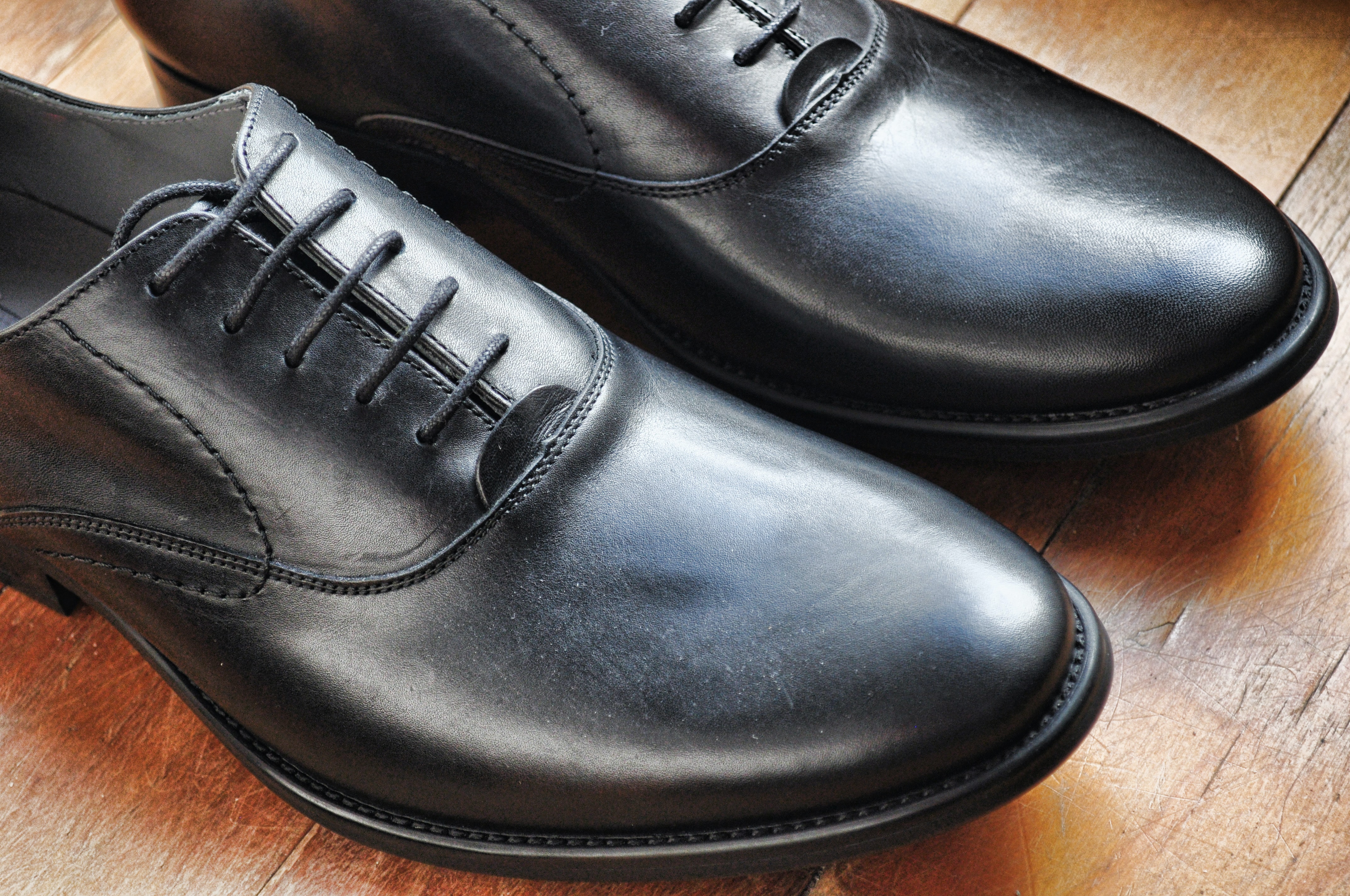 Pair of black dress shoes on top of wooden surface.