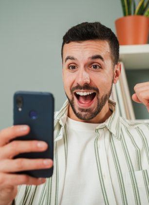 An overhead view of a sports betting setup, featuring a smartphone displaying betting odds, a notepad with handwritten notes, and a tabletop filled with sports paraphernalia, including a football, basketball, and racing information, symbolizing the excitement of sports wagering.
