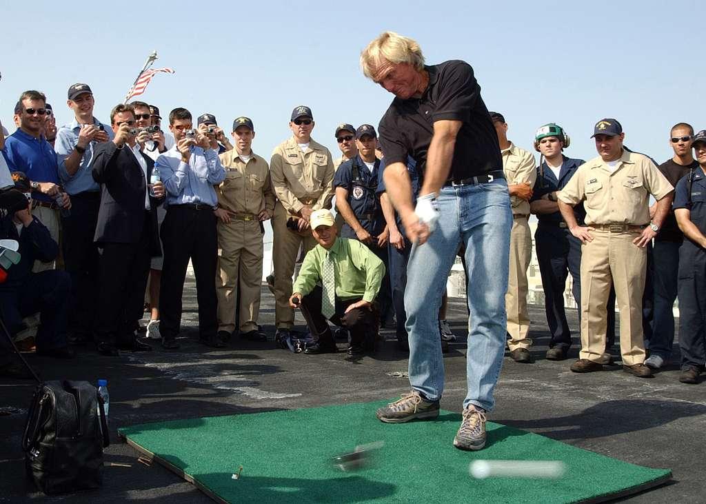 Greg Norman drives a golf ball off the flight deck