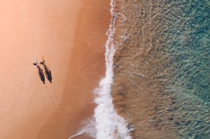 Drohnenaufnahme von zwei Surfern am Strand
