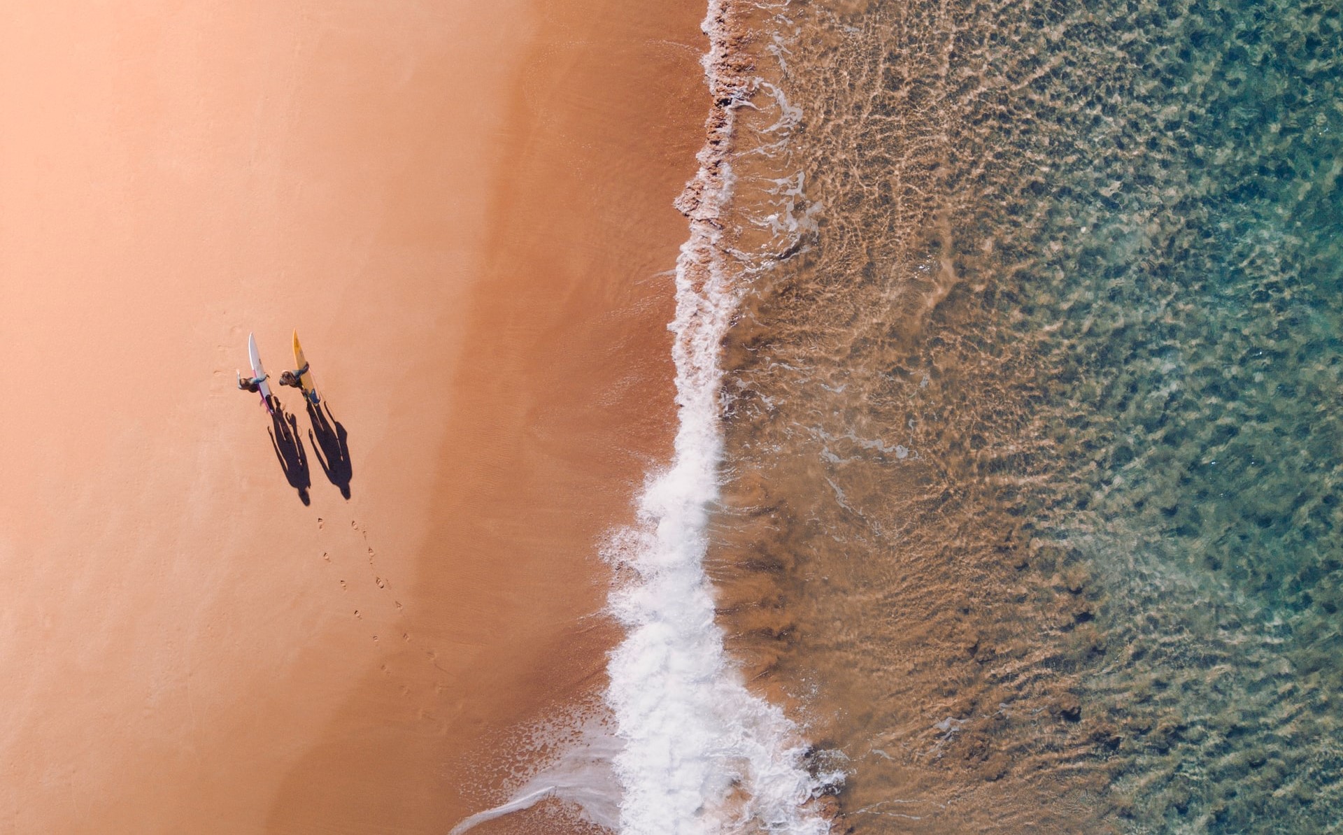 Drohnenaufnahme von zwei Surfern am Strand