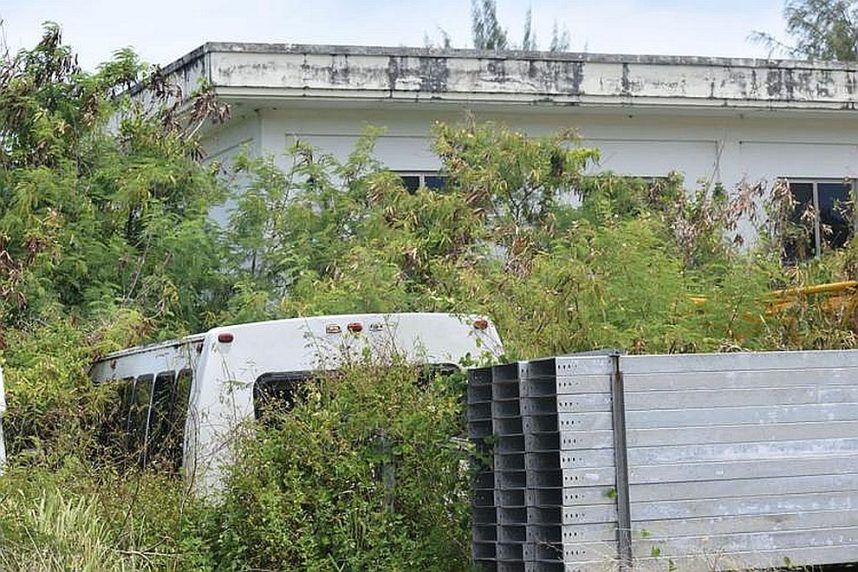 An IPI shuttle bus sits in overgrown vegetation