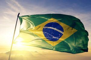 The sun shines behind the flag of Brazil
