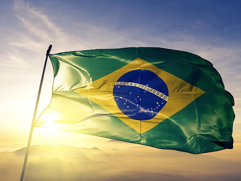 The sun shines behind the flag of Brazil