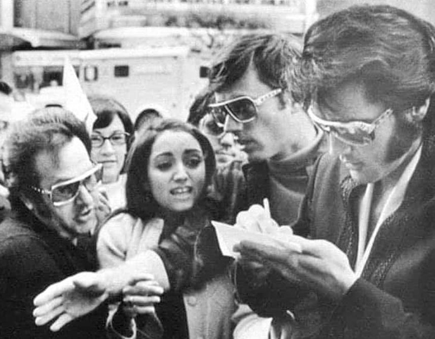 Elvis Presley signs autographs for a group of fans. 